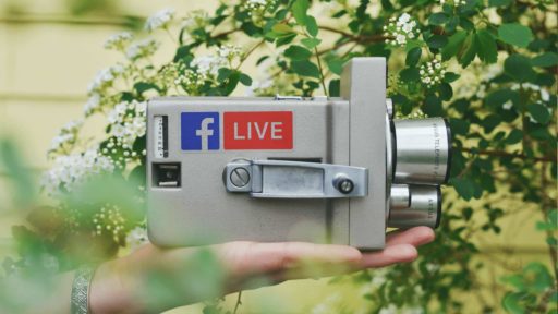 An old fashioned super 8 camera with a Facebook Live sticker on the side held up by someone's hand.